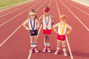 three children standing on a track field with medals from competitions