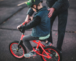 Man helps hold and steady his son as he learns to ride a bike.