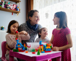 Nanny And Children Playing With Toys At Home