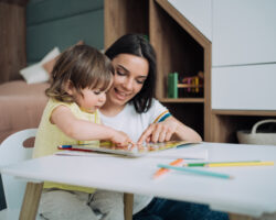 Little girl sitting at a table and coloring in a coloring book with her nanny.