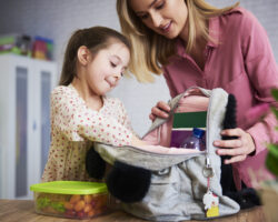 Nanny helping a young girl pack her backpack with lunch and school supplies during the back-to-school transition