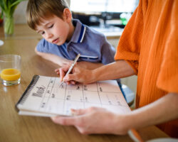 Family assistant updating a calendar while a child looks on, organizing health and school appointments for fall.