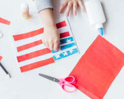 Child making a patriotic American flag craft with red, white, and blue paper for a Labor Day activity.