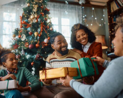 Family sharing holiday gifts with their nanny in a warmly decorated living room, celebrating the season together.