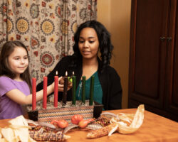 A caregiver helps a child light Kwanzaa candles while learning about holiday traditions.