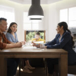 Parents meeting with their nanny at a dining table to discuss work goals and childcare needs during an annual review.