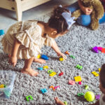 Young children play and clean up colorful toys together on a carpet, learning organization through play