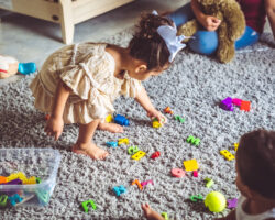 Young children play and clean up colorful toys together on a carpet, learning organization through play