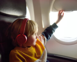 Child wearing headphones looks out airplane window, helping reduce sensory overload during travel