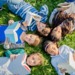 Children reading books outdoors during summer break, supporting learning and literacy development while preventing summer learning loss.