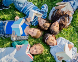 Children reading books outdoors during summer break, supporting learning and literacy development while preventing summer learning loss.