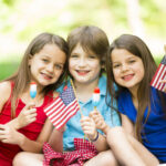 Children celebrating Memorial Day outdoors with American flags and patriotic treats during a festive summer gathering.