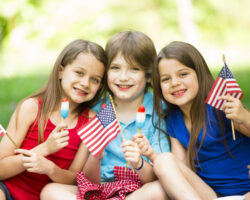Children celebrating Memorial Day outdoors with American flags and patriotic treats during a festive summer gathering.