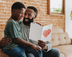 Father and child sharing a homemade Father’s Day card while spending quality time together at home, celebrating a simple and meaningful Father’s Day.
